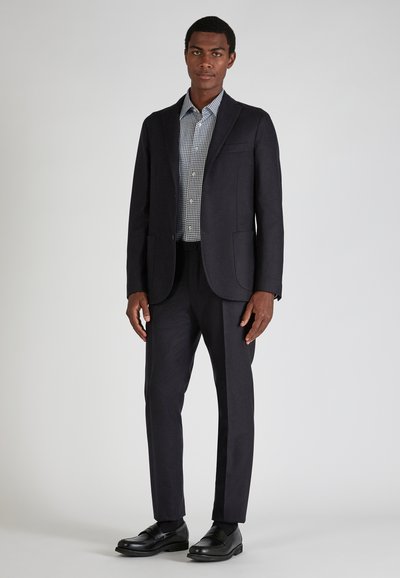 Ciemnoniebieska marynarka w garniturze z dopasowanymi spodniami, zestawiona z jasnoniebieską koszulą w białą kratkę. Gładka faktura i dopasowany krój. Czarne buty.
