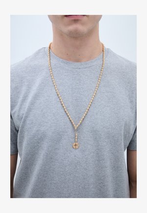 Man draagt een lichtgrijs T-shirt met een gouden kralenrosarium met een kruishanger die op borsthoogte hangt.