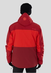 Rot und kastanienbraun gestreifte Mehrpaneel-Jacke mit Kapuze, mit einem Logo auf der Rückseite, hergestellt aus einem glatten, wetterfesten Material.