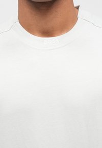 Λευκό βαμβακερό t-shirt με στρογγυλή λαιμόκοψη, με διακριτικό ανάγλυφο λογότυπο "BOSS" κατά μήκος του γιακά. Λείο ύφασμα, μίνιμαλ σχεδιασμός.