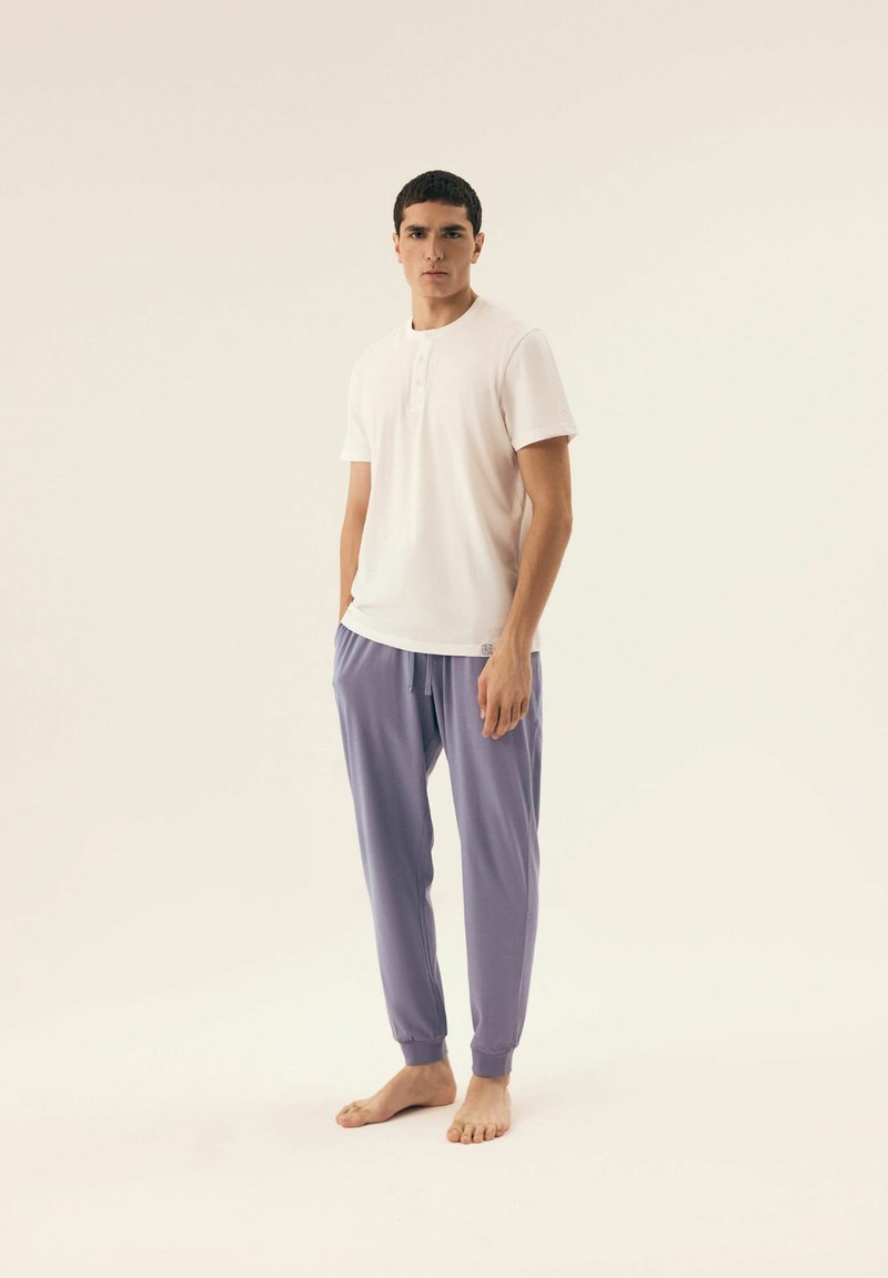 White short-sleeve henley shirt with three buttons paired with light lavender jogger pants featuring an elastic waistband and cuffs.