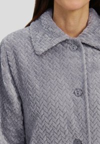 Chaqueta de piel sintética gris con un patrón de espiga texturizado, con un cuello tipo solapa y botones redondos para el cierre.