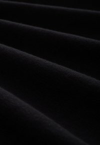 Schwarzer Stoff mit einer glatten Textur, der subtile Wellen zeigt. Das Material wirkt weich und leicht dehnbar, was auf Vielseitigkeit hinweist.