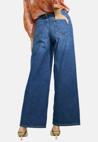 Korkeavyötäröiset, leveät denim-farkut keskisinisessä värissä, joissa on sileä pinta ja klassinen viisi-taskumalli, ja joissa on hieman räsymäinen helmamalli.