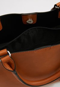 Brązowa skórzana torebka z czarną tkaninową wyściółką, widoczna kieszeń na zamek błyskawiczny oraz magnetyczne zapięcie, pokazana z widoku otwarcia od góry.