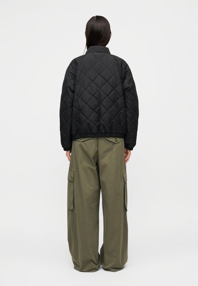 Μαύρο καπιτονέ μπουφάν με ψηλό γιακά και ελαστική μέση, σε συνδυασμό με χαλαρά χακί παντελόνια cargo με πλαϊνές τσέπες.