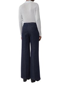 Pantaloni in denim a gamba larga di un blu scuro con una texture liscia, dotati di tasche laterali e vita alta, abbinati a un top grigio chiaro a maniche lunghe.