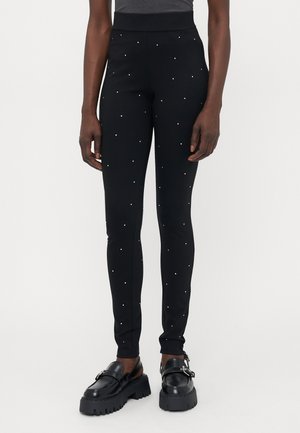 Sorte leggings med høj talje, prydet med spredte sølvnitter, lavet af strækbart stof, med en tætsiddende pasform og en glat tekstur.