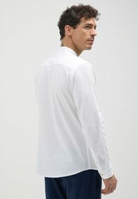 Camicia bianca a maniche lunghe realizzata in tessuto leggero, con colletto classico e polsini con bottoni; texture liscia con vestibilità comoda.