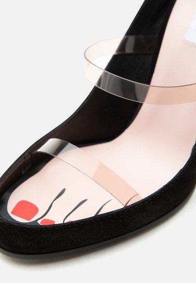 Μαύρο παπούτσι ανοιχτής μύτης με διαφανή πλαστικά λουράκια και εσωτερική σόλα που απεικονίζει ένα ζωγραφισμένο πόδι με κόκκινα νύχια.