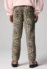 Pantalones de cintura alta con estampado de leopardo, de fondo beige y detalles en negro, con bolsillos tipo parche y un corte relajado, combinados con sandalias gruesas.