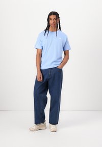 T-shirt en coton bleu clair à manches courtes, associé à un jean en denim bleu foncé ample et des chaussures de sport beiges. Design simple, sans motifs visibles.