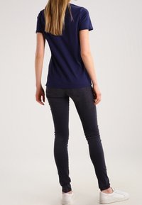 Camiseta de manga corta azul marino combinada con jeans oscuros ajustados. La camiseta tiene un escote redondo y un corte holgado. Zapatillas blancas.