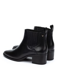 Un par de botines de cuero negro con tacones de bloque, paneles elásticos laterales y lengüetas en la parte trasera, mostrados sobre un fondo blanco.