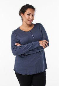 Langärmliges, marineblaues Oberteil aus weichem Stoff; verfügt über einen runden Halsausschnitt, eine Knopfleiste und gewellte Säume an Hemd und Ärmeln.