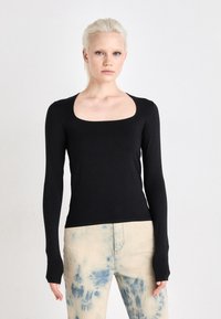 Svart langermet topp med firkantet utringning, tettsittende design og elastisk tekstur, sammen med lyseblå tie-dye jeans.