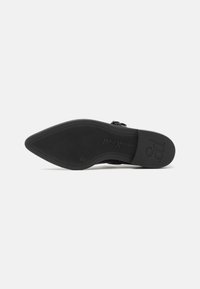 Black shoe sole with a pointed shape, featuring a textured rubber grip and embossed logo. Smooth edges and minimalist design.