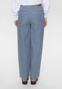 Pantalons larges à rayures bleues et blanches avec deux poches arrière et un patch en cuir marron au niveau de la taille. Tissu en coton lisse.