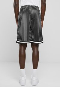 Shorts rayés noir et blanc avec une taille élastique et des accents blancs sur les côtés, fabriqués en tissu léger, présentant une coupe décontractée.