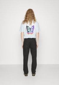 Light blue t-shirt with a butterfly graphic in shades of blue and purple on the back, paired with black pants.