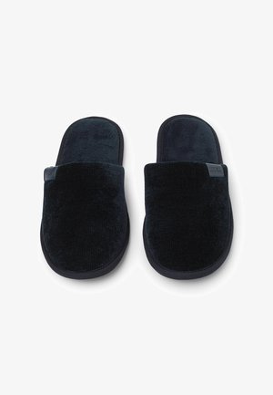 Schwarze Corduroy-Hausschuhe mit einem plüschigen Obermaterial und einem weichen Innenfutter. Sie verfügen über eine runde Spitze und eine dicke, strukturierte Sohle für zusätzlichen Komfort.