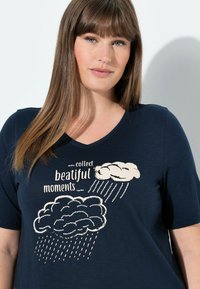 Mørkeblå t-shirt i blødt materiale med V-hals, pyntet med cremefarvede sky-grafikker og teksten "collect beautiful moments."