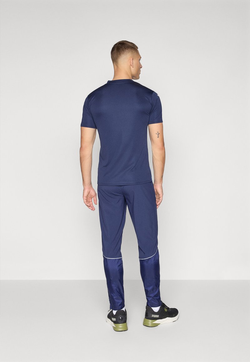 Conjunto deportivo en azul marino que incluye una camiseta de manga corta y pantalones ajustados. Tejido suave, con un brillo sutil y detalles reflectantes en los pantalones. Zapatillas negras.