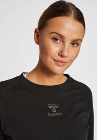 Svart sweatshirt med rund halsringning, prydd med en diskret grå logotyp på bröstet. Tyget verkar mjukt med en slät struktur.