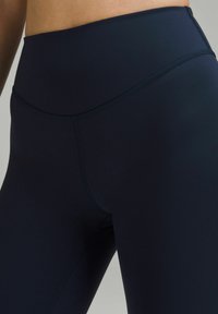 Hoch geschnittene marineblaue Leggings aus dehnbarem Material mit flachen Nähten und einem glatten, matten Finish. Hat ein einfaches, schlankes Design.