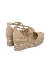 Chaussures compensées en suede beige avec des sangles croisées, semelle en jute tissée, accents métalliques et une plateforme texturée et superposée.