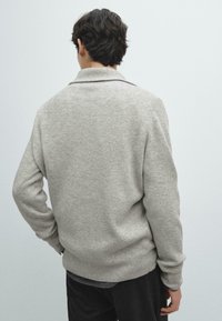 Grauer Rippstrickpullover mit hohem Kragen und langen Ärmeln, mit lockerer Passform und weicher Textur, von hinten betrachtet.