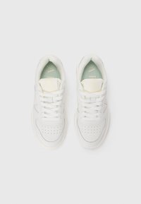 White sneakers with a smooth leather upper, padded tongue, and textured mesh lining. Features perforations near the toe and accent stitching.