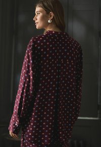 Koszula w burgundowym kolorze z wzorem w małe niebieskie i czerwone kształty geometryczne, z długimi rękawami, kołnierzykiem i zapinanymi mankietami. Miękka tkanina, luźny krój.