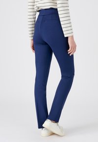 Marineblauwe skinny broek met een hoge taille, zijzakken en een gladde textuur, gecombineerd met witte sneakers met zilveren accenten.