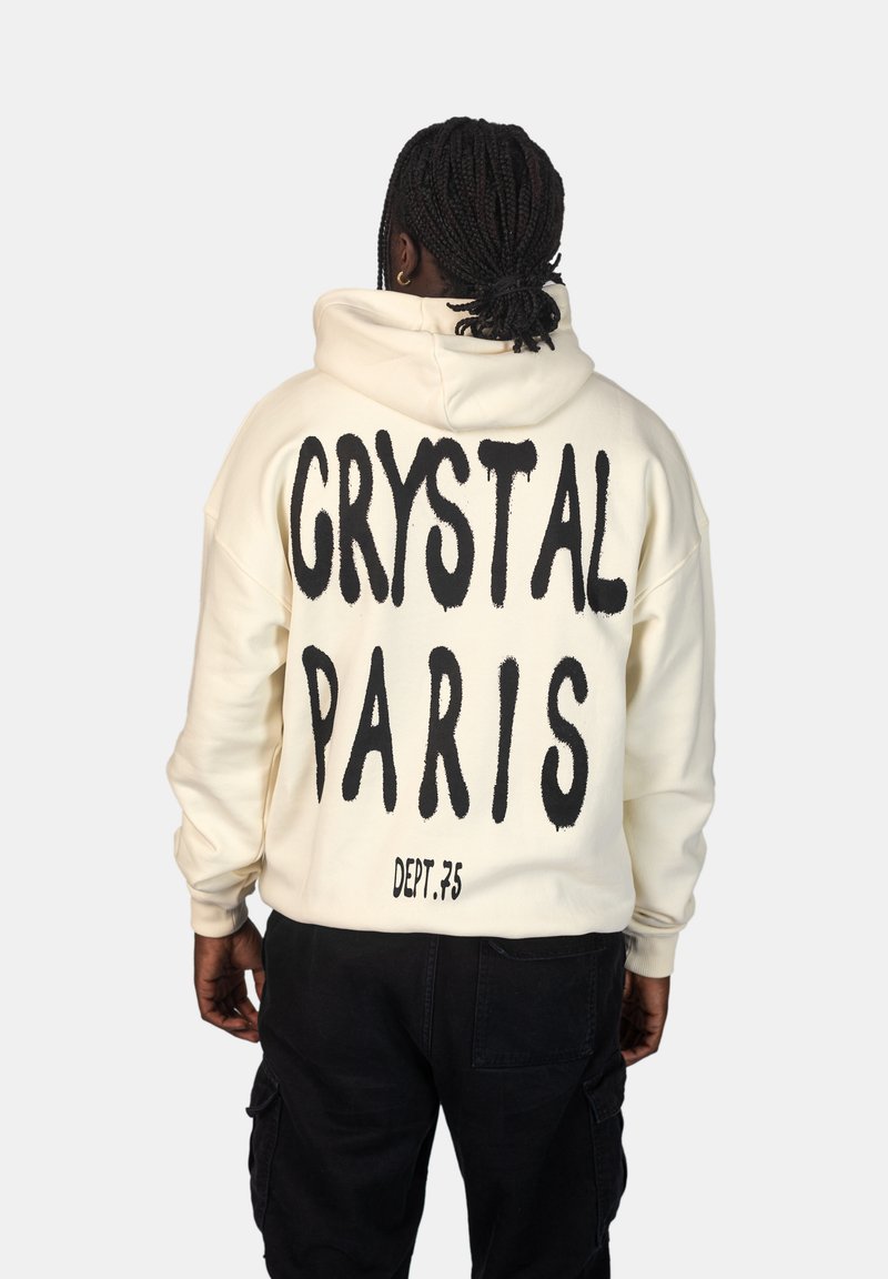 Felpa crema con testo in bold nero che recita "CRYSTAL PARIS" e "DEPT.75" sul retro. Progettata con una vestibilità comoda e cappuccio.
