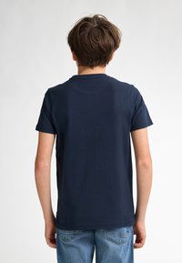 Marineblå bomulds T-shirt med korte ærmer, rund halsudskæring og en glat tekstur. Båret med lyseblå denim jeans.