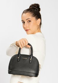 Borsa a mano in pelle nera con finitura testurizzata, forma rotonda, doppi manici, hardware dorato e chiusura con zip. Logo visibile.
