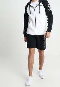 Hooded zip-jacka i svart och vitt med kontrasterande design. Svarta shorts med vita logotyper. Sneakers fulländar den atletiska stilen.