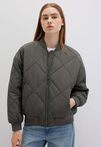 Giacca bomber imbottita verde oliva con chiusura a zip, polsini a coste e una vestibilità leggermente oversize. Tessuto morbido e leggero.