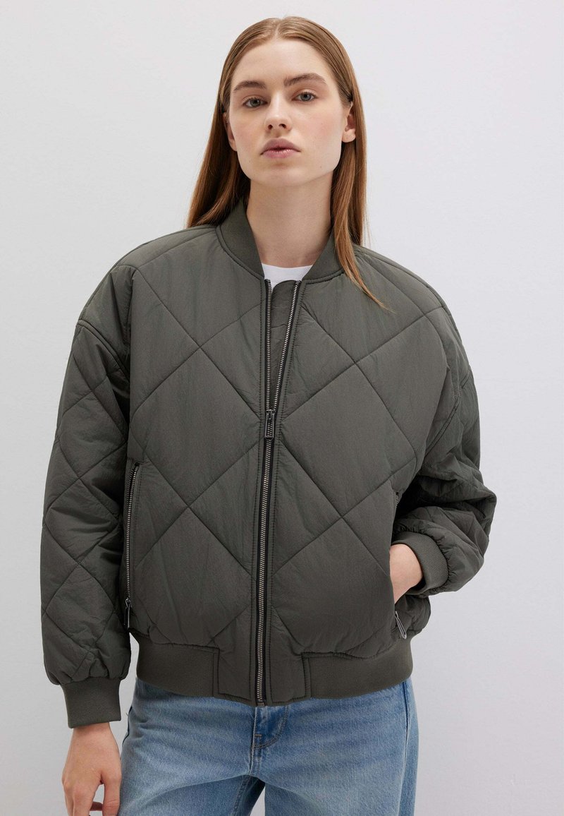 Giacca bomber imbottita verde oliva con chiusura a zip, polsini a coste e una vestibilità leggermente oversize. Tessuto morbido e leggero.