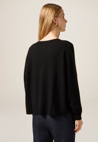 Schwarzer Strickpullover mit lockerem Sitz, gerippten Bündchen und Saum. Weiche Textur mit rundem Ausschnitt und mehrschichtigem Rückendesign.