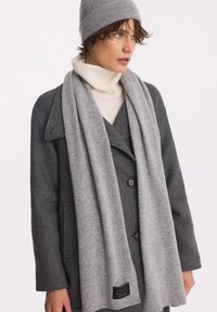Szary wełniany płaszcz o podwójnym zapięciu, w połączeniu z jasnoszarym szalikiem i pasującą czapką, wszystko w miękkiej teksturze.