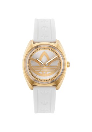 Montre dorée avec un bracelet en caoutchouc blanc. Le cadran rond présente un fond argenté et un logo trefoil adidas en or bien en évidence.
