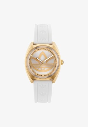 Reloj dorado con correa de goma blanca. La esfera redonda presenta un fondo plateado y un prominente logotipo de trébol dorado de adidas.