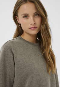 Harmaa, teksturoitu pitkähihainen paita, jossa on pyöreä kaula-aukko. Sileä kangas, rento istuvuus ja hienovarainen ommel yksityiskohta olkapäillä.