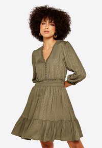Olivgrünes Kleid mit strukturiertem Rautenmuster, V-Ausschnitt, Knopfdetails, elastischem Taillenbund und geschichteter Rockpartie. 3/4 Puffärmel.