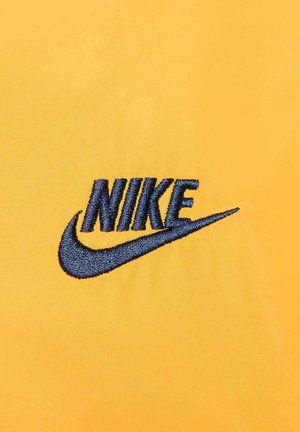 Tela amarilla con un logotipo "NIKE" bordado en azul marino y el swoosh. La textura es suave, y el diseño es simple y audaz.