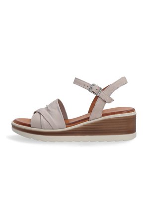 Beige leather wedge sandal with a knotted front design, adjustable ankle strap, and a textured midsole. White outsole with traction.