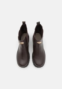 Botas de cuero marrón hasta el tobillo con un acabado suave, punta redonda, suela de goma negra y herrajes dorados decorativos en los laterales.