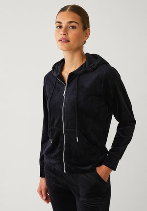 Zwarte velours zip-up hoodie met een gevoerde capuchon, voorzakken en trekkoorden. Heeft een soepele textuur en zilverkleurige ritshardware.